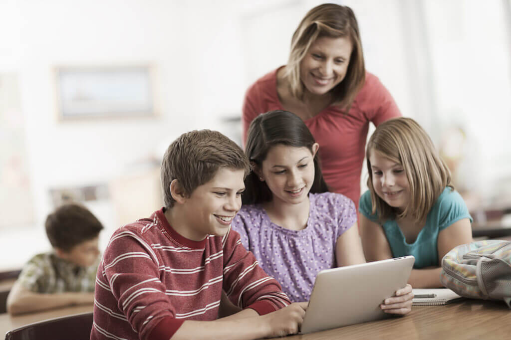 teacher and three school children looking at a digital device.